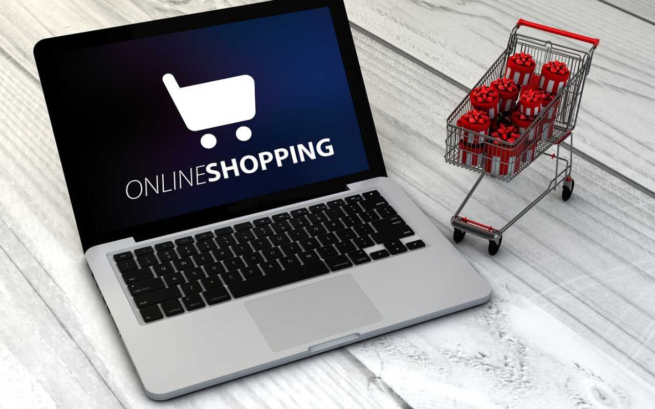 Laptop na kojem se nalazi online kupovina, a pored njega su mala kolica sa poklonima