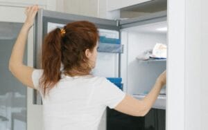 Žena u beloj majici i farmerkama otvara zamrzivač