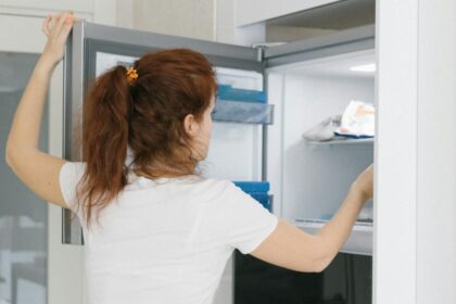 Žena u beloj majici i farmerkama otvara zamrzivač