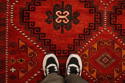 Osoba stoji na tradicionalnom crvenom tepihu sa raznim šarama i motivima