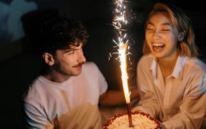 Momak i devojka drže rođendansku tortu sa prskalicom i smeju se