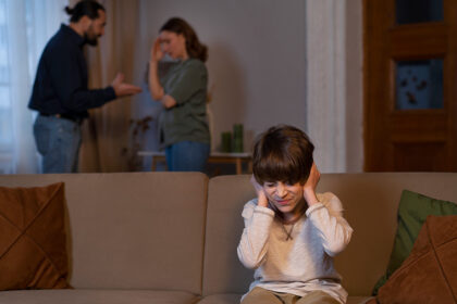 Roditelji se svađaju, a dete sedi na trosedu sa rukama preko ušiju.