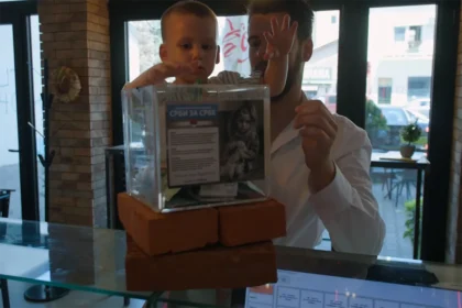 Dete ubacuje novac u kutiju za donacije Humanitarne organizacije Srbi za Srbe