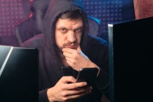 Muškarac sa mobilnim telefonom sedi ispred dva monitora