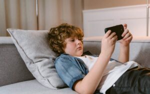 Dečak leži na kauču i igra igrice na telefonu