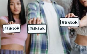 Dve devojke i jedan dečko drže telefon na kojem piše #Tiktok
