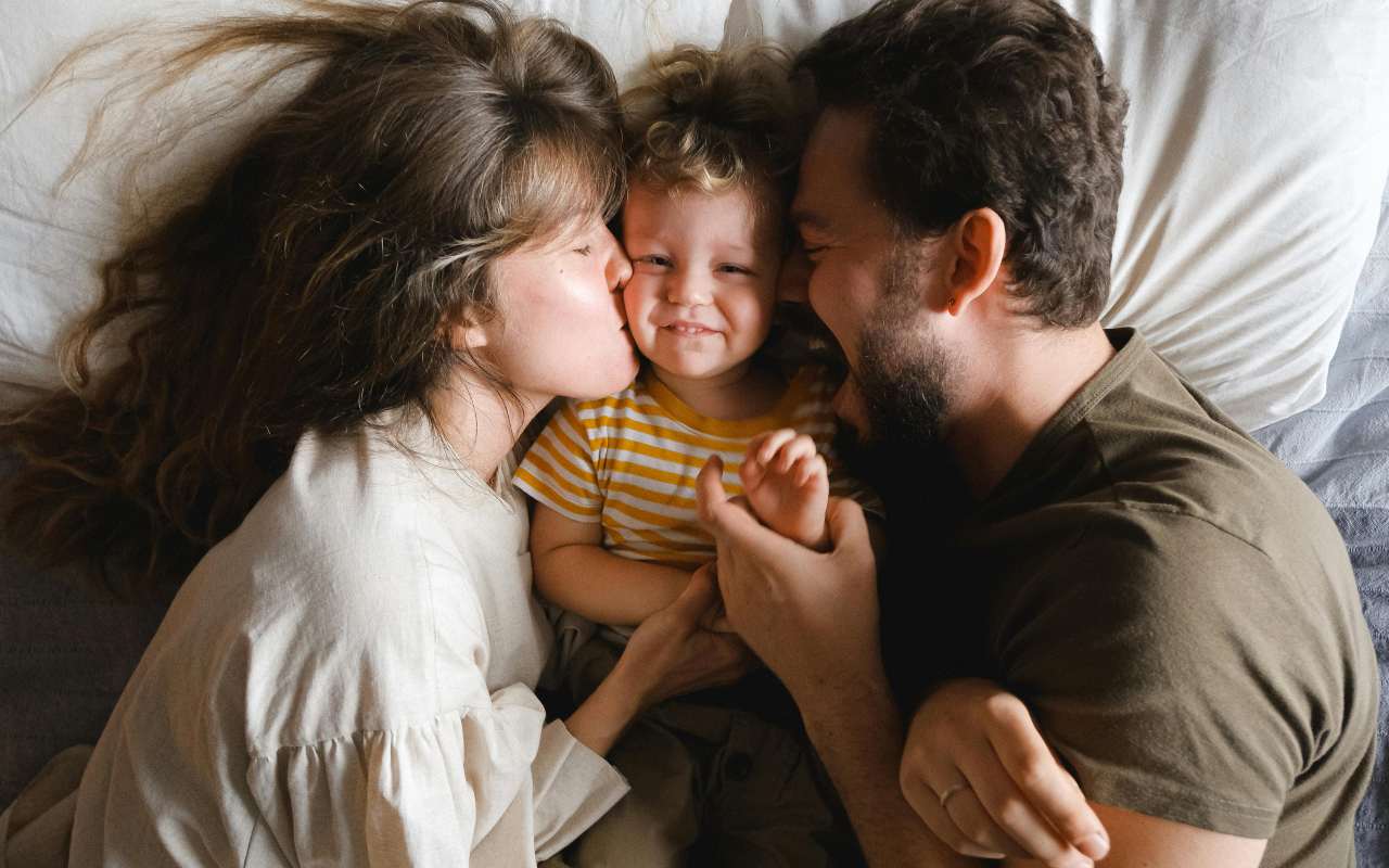 Dete leži između roditelja na krevetu