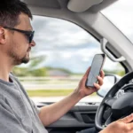 Muškarac vozi automobil i koristi mobilni telefon