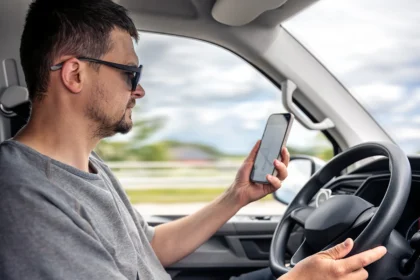 Muškarac vozi automobil i koristi mobilni telefon