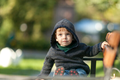 Dečak u džemperu sa kapuljačom sedi na klupi