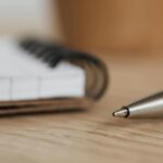 Metalni vrh hemijske olovke u prvom planu pored žičane sveske