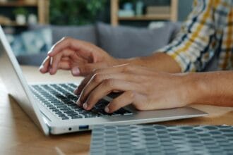 Ruke kucaju na tastaturi laptopa, osoba nosi kariranu košulju