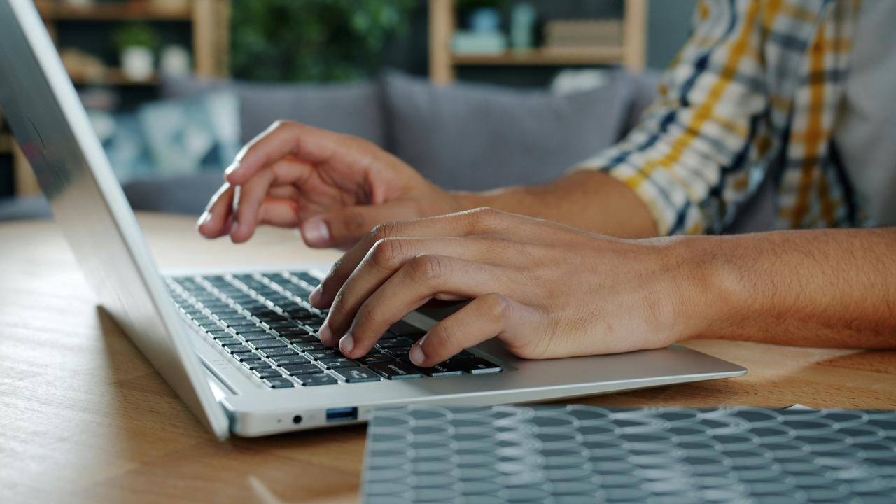 Ruke kucaju na tastaturi laptopa, osoba nosi kariranu košulju