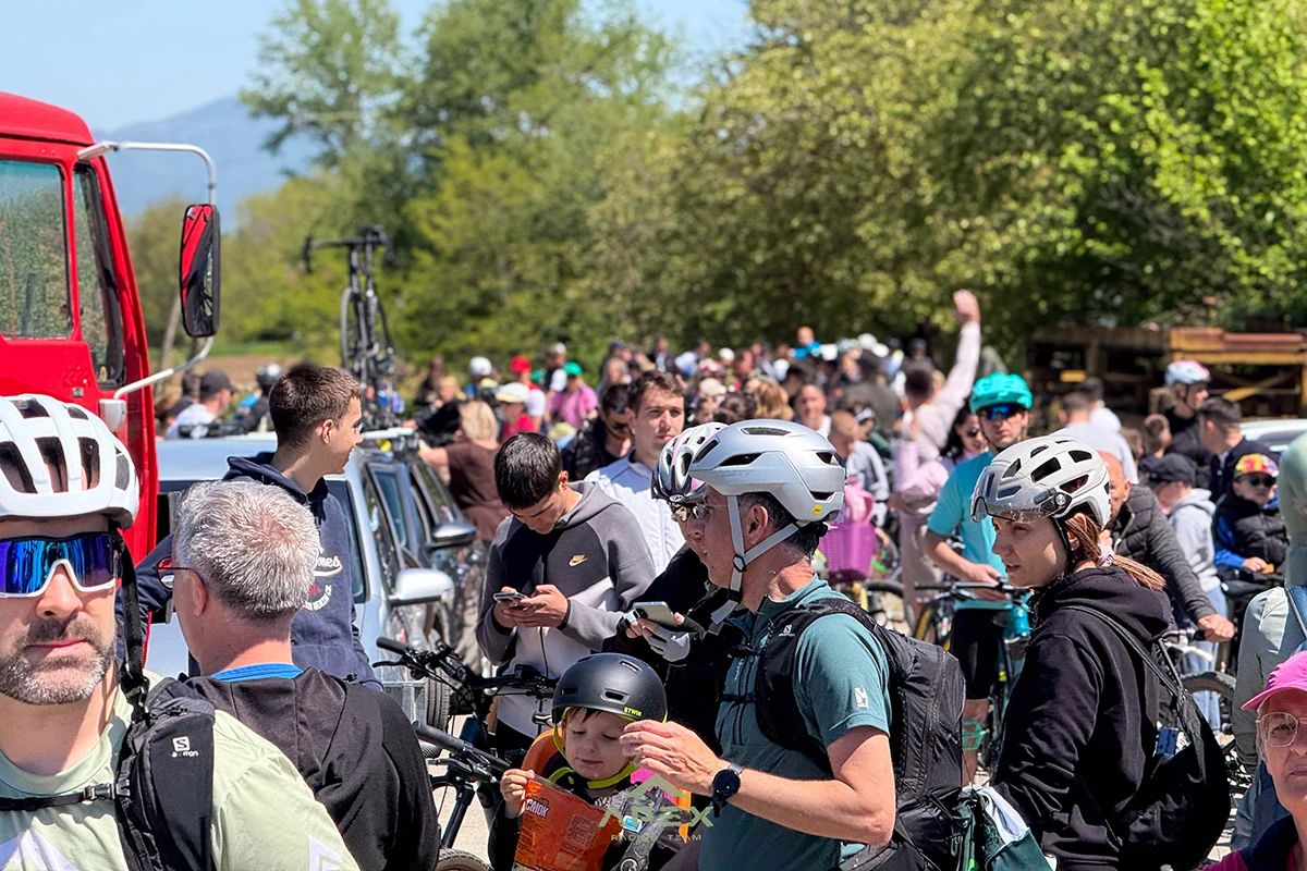 Crowd of cyclists and spectators gathered outdoors on a sunny day, many wearing helmets with bicycles in the background.