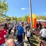 Crowd of people at an outdoor cycling event with bikes lined up and an orange inflatable arch in the background