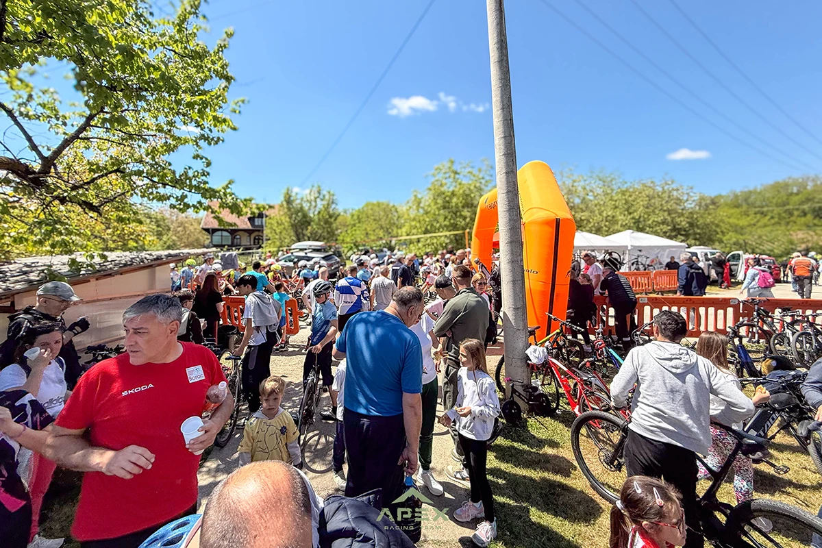 Crowd of people at an outdoor cycling event with bikes lined up and an orange inflatable arch in the background