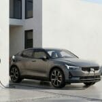 Električni automobil priključen na zidnu stanicu za punjenje ispred moderne kuće