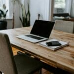 Otvoren laptop na drvenom stolu pored sveske i pametnog telefona