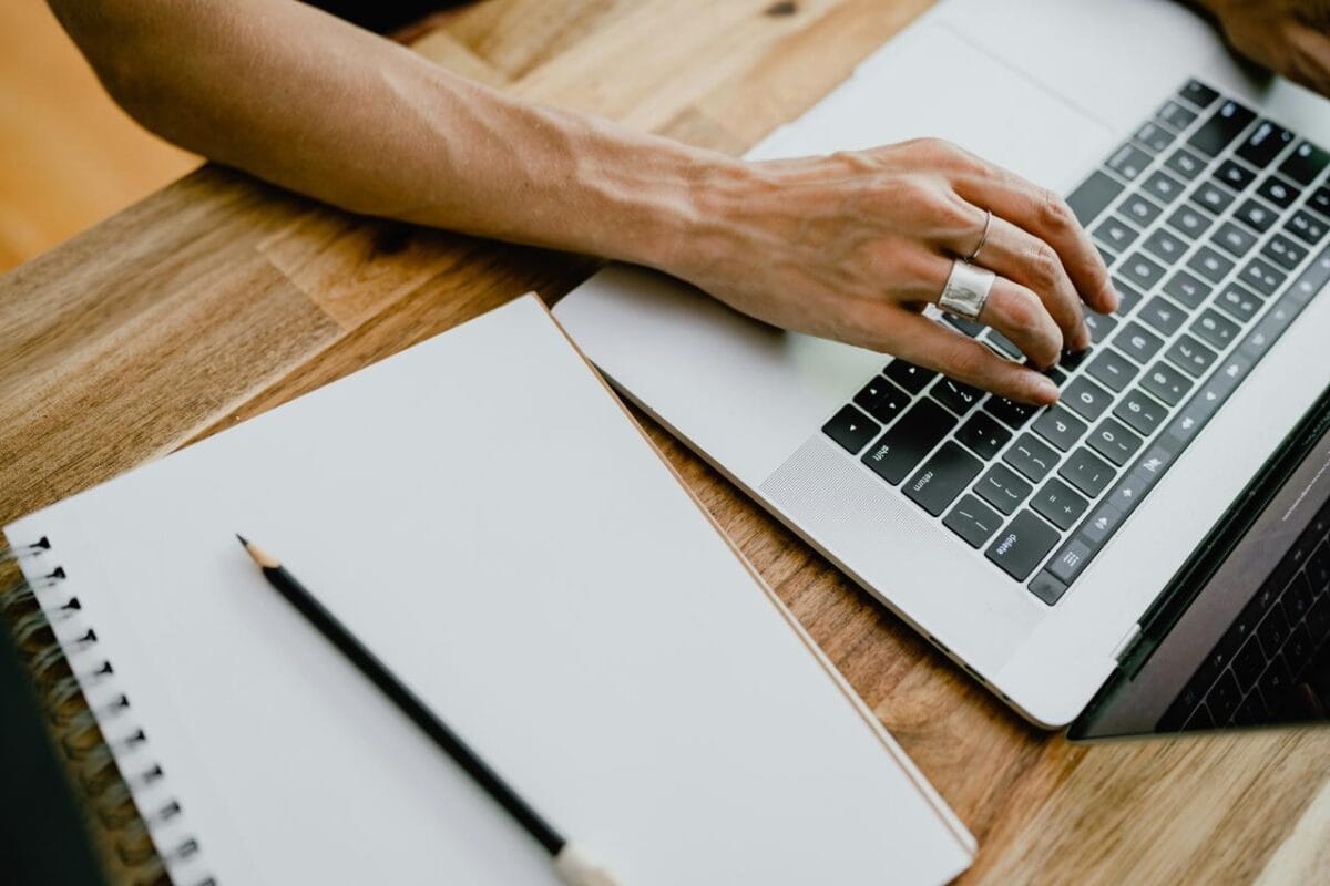 • N2 portal Ruka sa prstenom piše na laptop tastaturi pored otvorene sveske i olovke