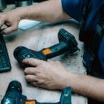 Majstor jednom rukom drži šrafilicu na stolu, dok drugom kuca na tastaturi