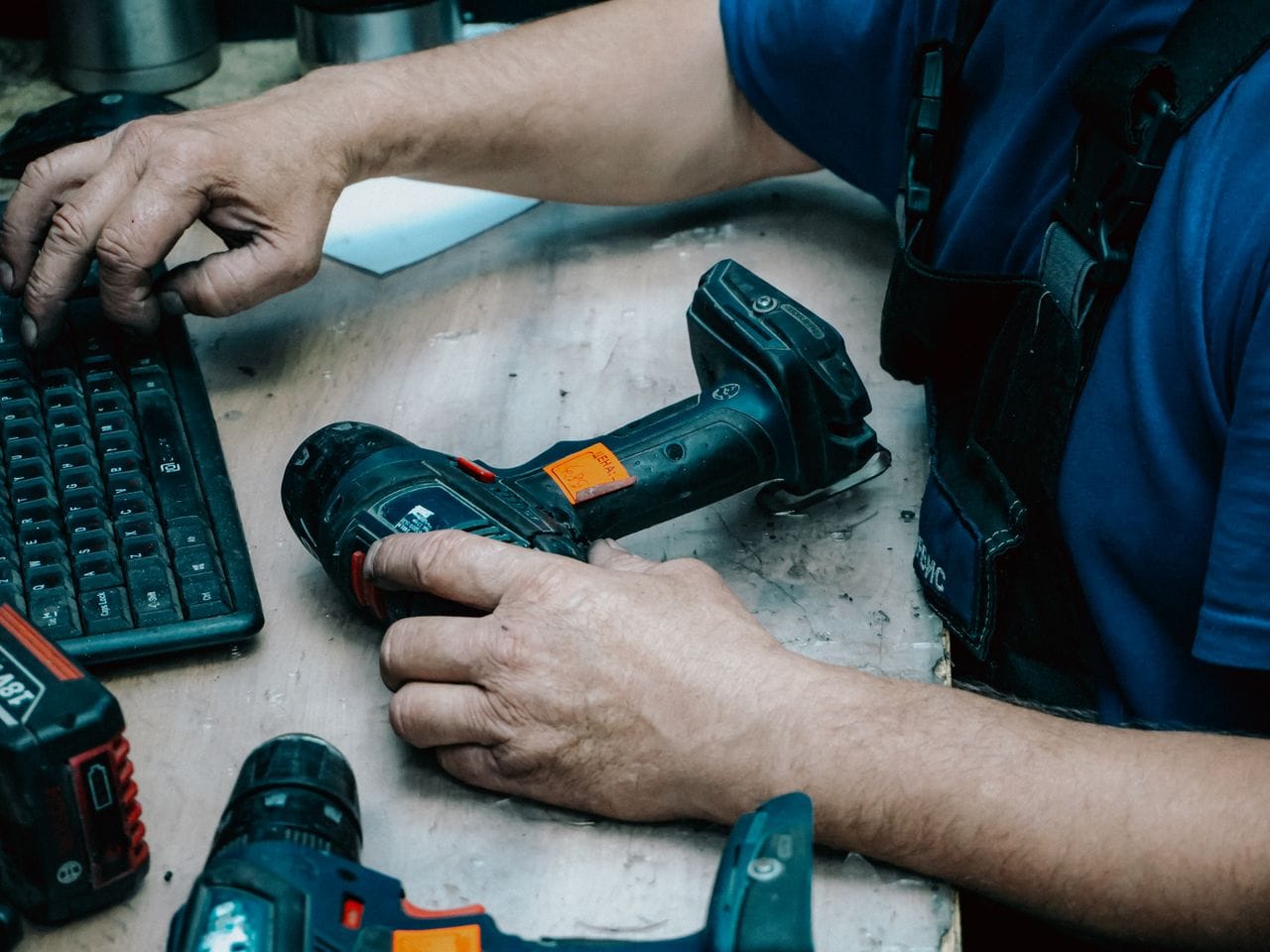 Majstor jednom rukom drži šrafilicu na stolu, dok drugom kuca na tastaturi